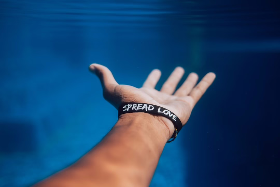 A man underwater extending his hand with a bracelet that says "Spread Love"