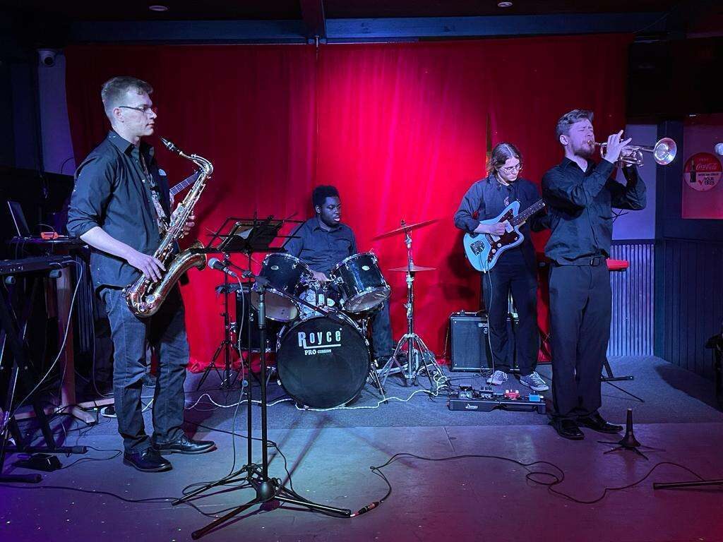 Trumpeter Cesar Vazquez, guitarist Caio Cordeiro, drummer Jeremiah Dillard, and saxophonist Dorian Bryja performing on stage.